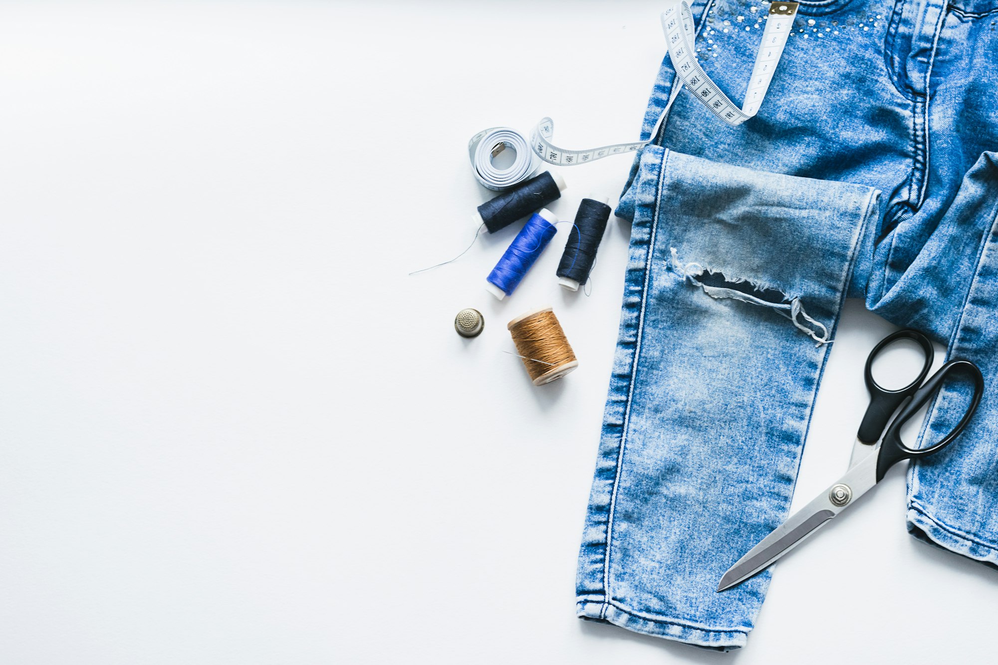 Handicraft clothing repair. Ripped blue jeans sewing accessories white background