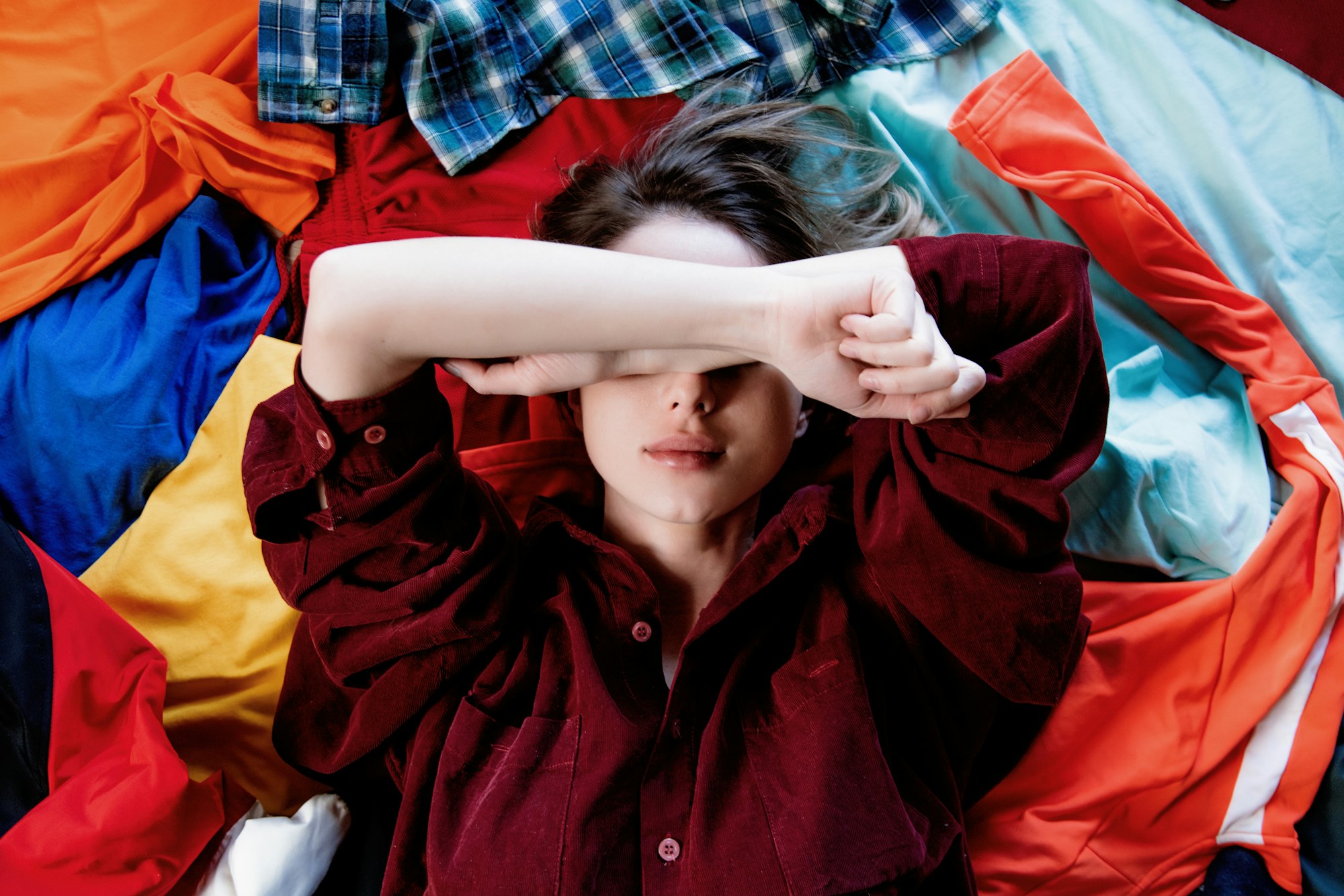 Upset woman keep hands over head and lying on clothes.